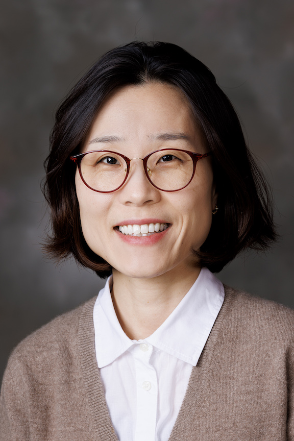 Dr. Saet-Byul Kim, smiling, wearing a white collared shirt and grey cardigan in front of a dark grey background.