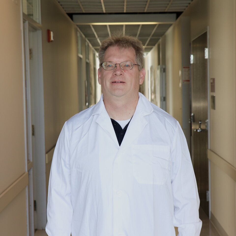 John McKendry stands in a partially dark hallway wearing a white coat.