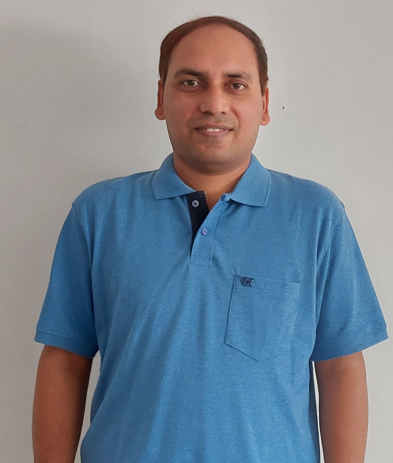 Sudeep Tiwari, pictured smiling against a light colored wall in a light blue, short sleeved shirt.