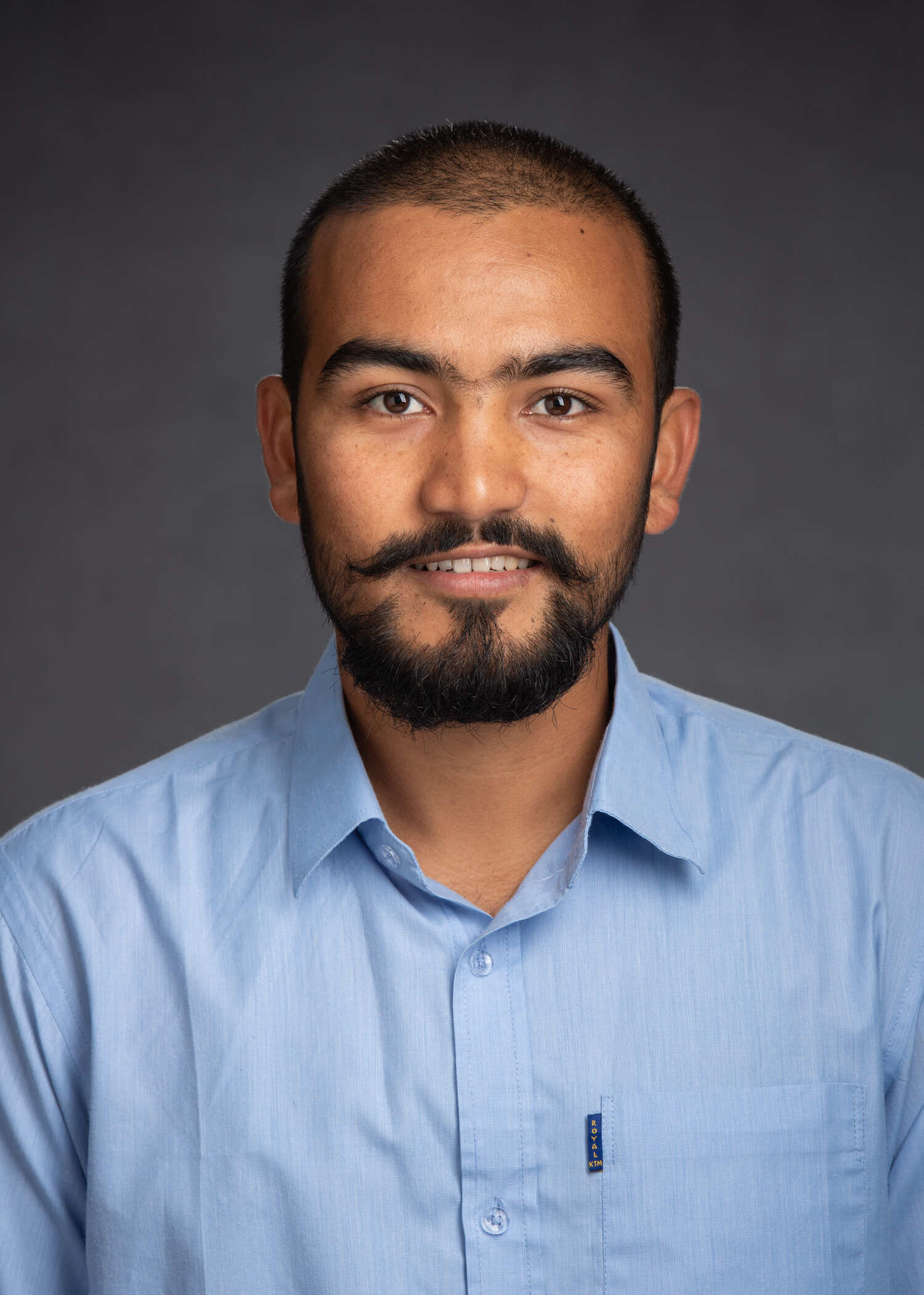 Bhanu Dangi, smiling, in a light blue shirt in front of a dark gray background.