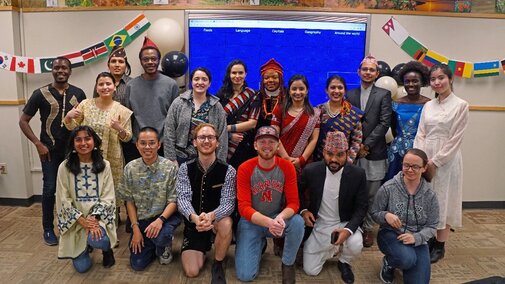 Plant pathology graduate and undergraduate students stand in front of a monitor, many of them wearing culturally significant attire