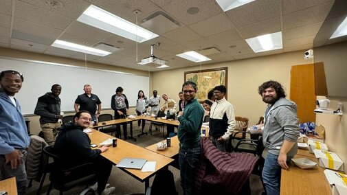 Students smile for the camera in a conference room during a lunch meeting