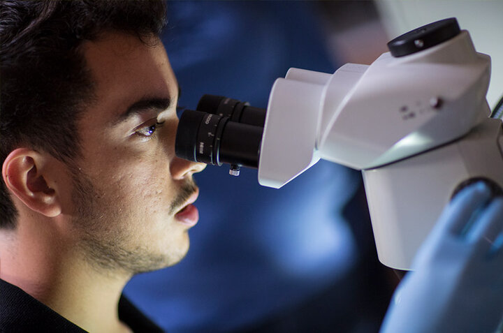 A student looks through a microscope in a darkened room